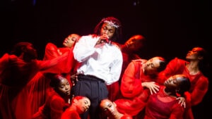 Kendrick Lamar performing music on stage at Glastonbury 2022 wearing white surrounded by several backup dancers wearing red